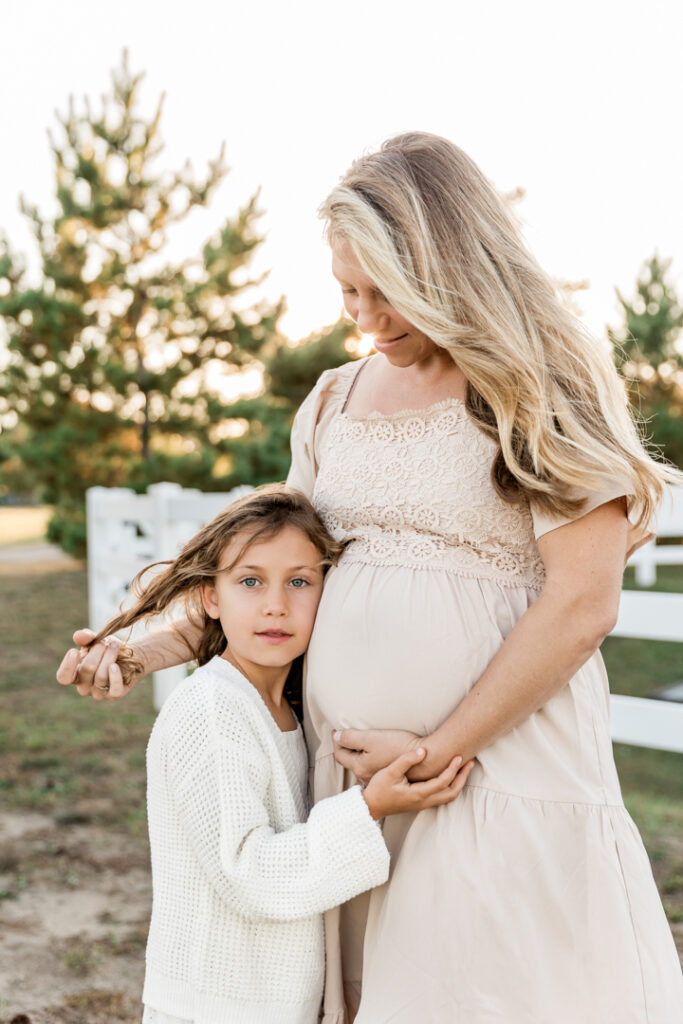 pregnant woman standing in golden light smiling at her daughter
