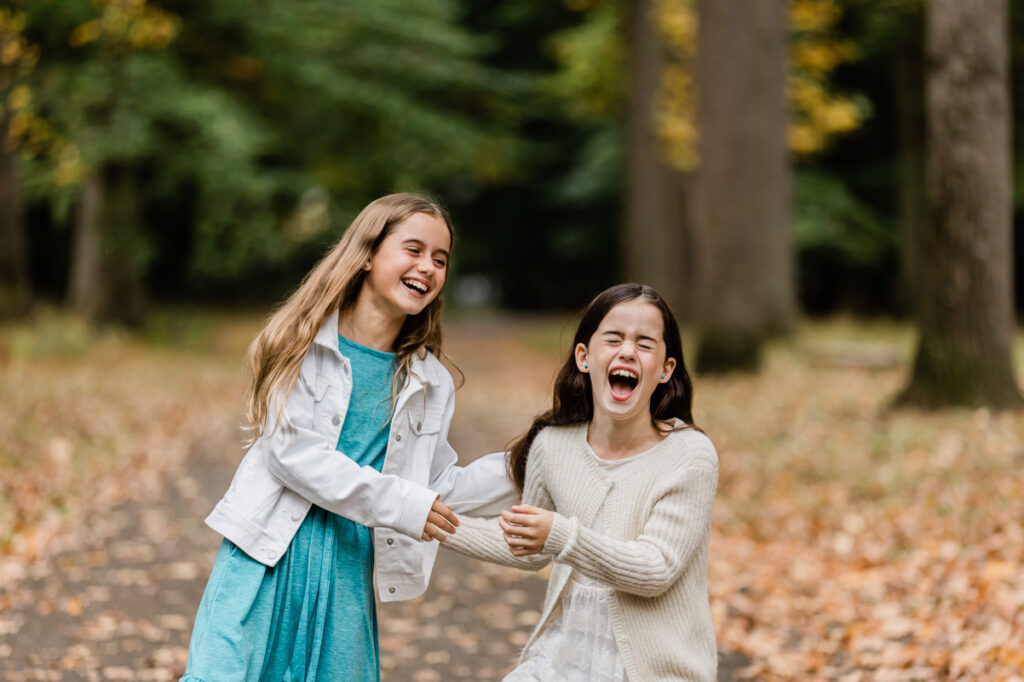 Sisters laughing during fall sibling photo session in Tamaques Park, Westfield, NJ
