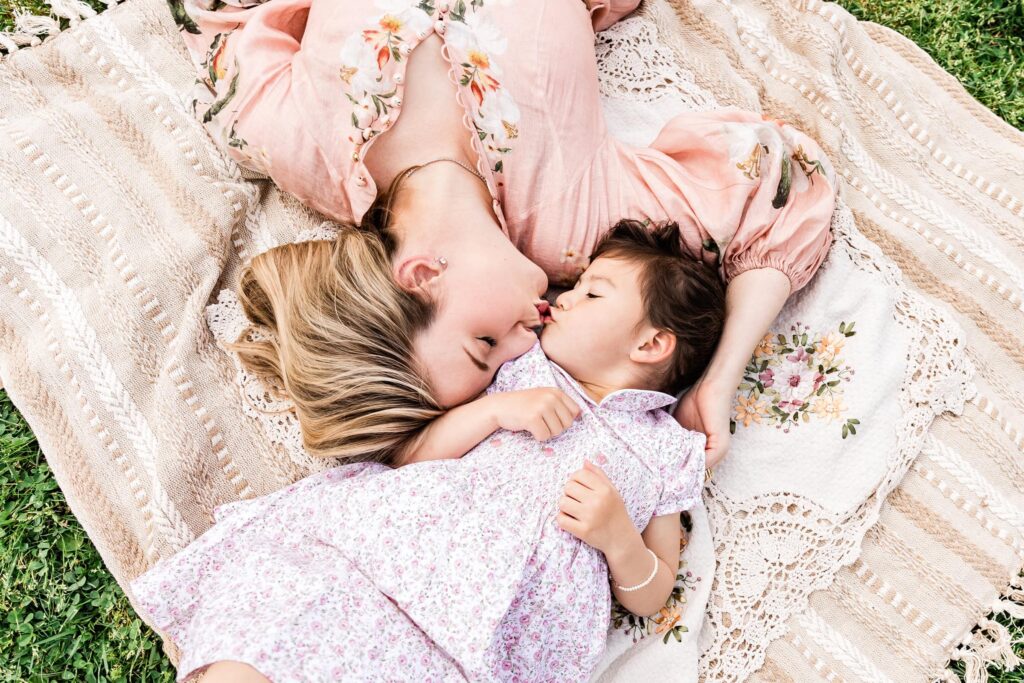 Mother and daughter laying on a blanket in a sweet moment while they kiss with eyes closed