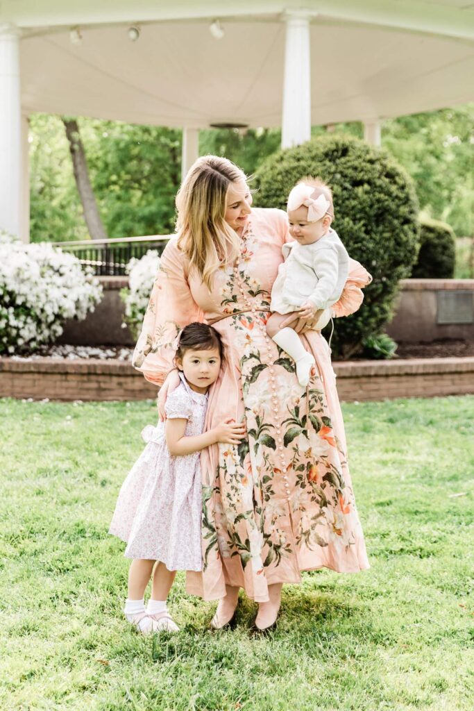 Mother stands holding baby girl and little girl snuggles close illustrating perfect colors to wear for family photos in springtime