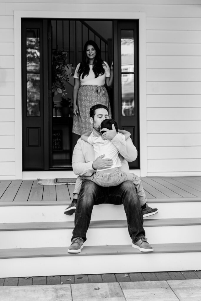 black and white image of father kissing his son's forehead as they sit together on front porch