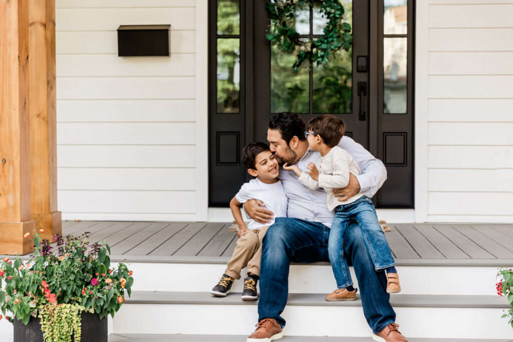 father embracing his little boys as they sit on their front porch