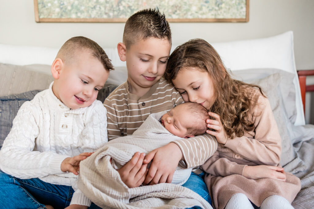 Siblings sitting on bed while little girl kisses her baby brother