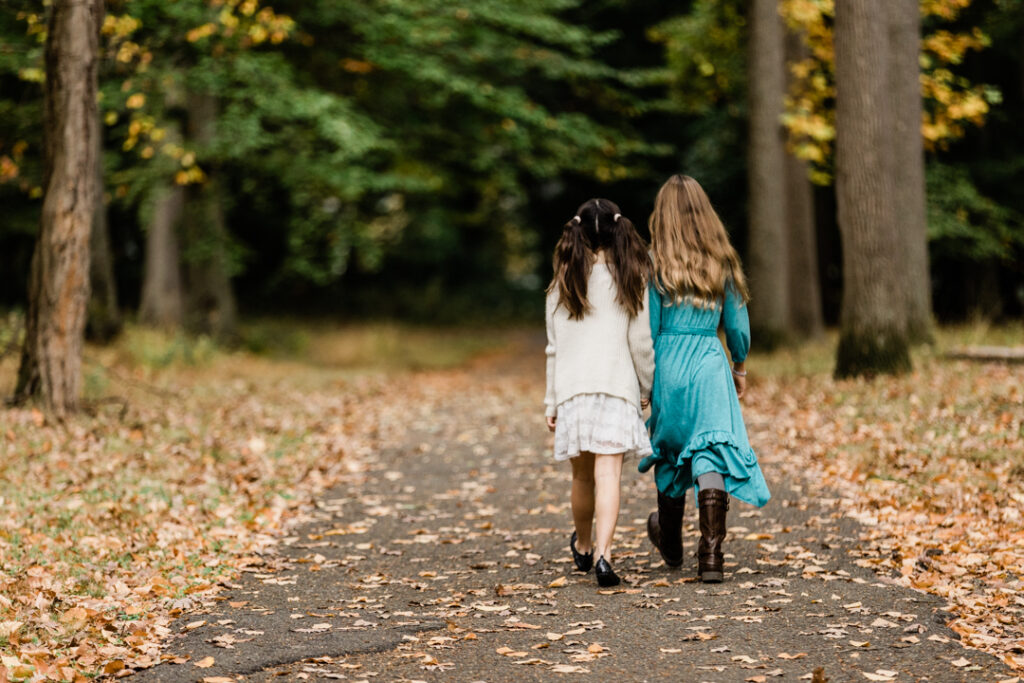 Teen girls holding hands and walking in the woods in fall