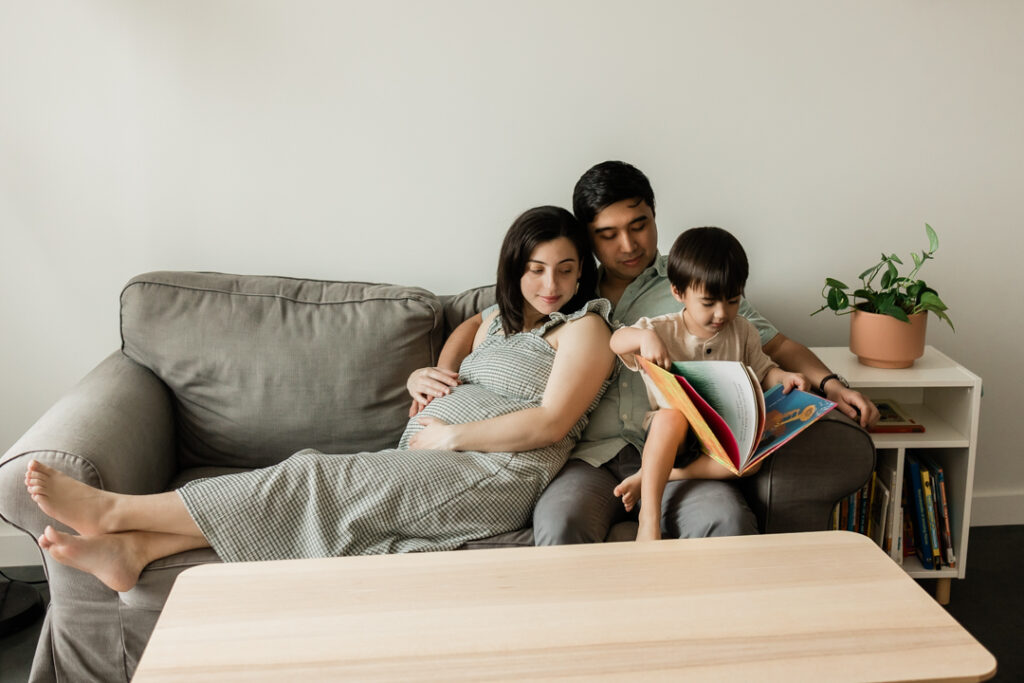 Pregnant mom cuddling with man and toddler on couch during in-home maternity session in NJ