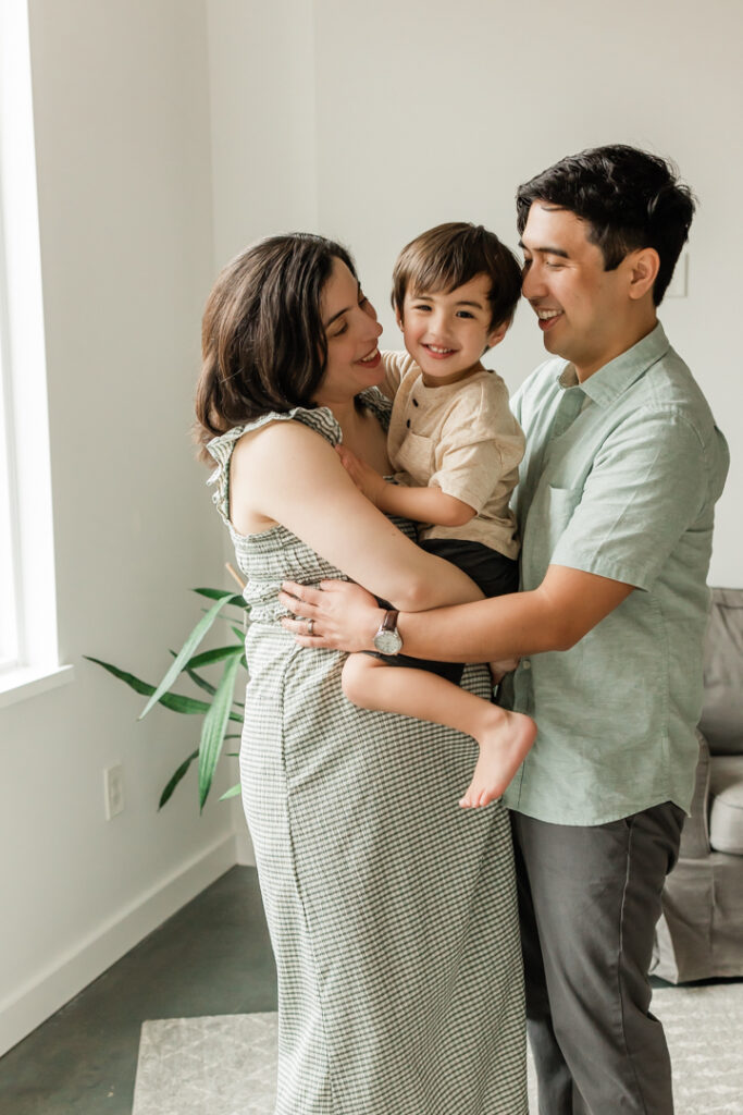 Pregnant woman holding toddler and smiling while man embraces them