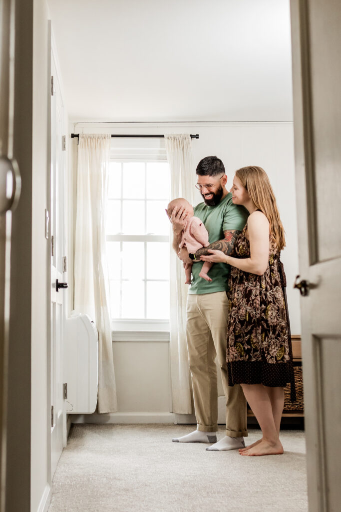 couple smiling lovingly at newborn baby during in-home photoshoot
