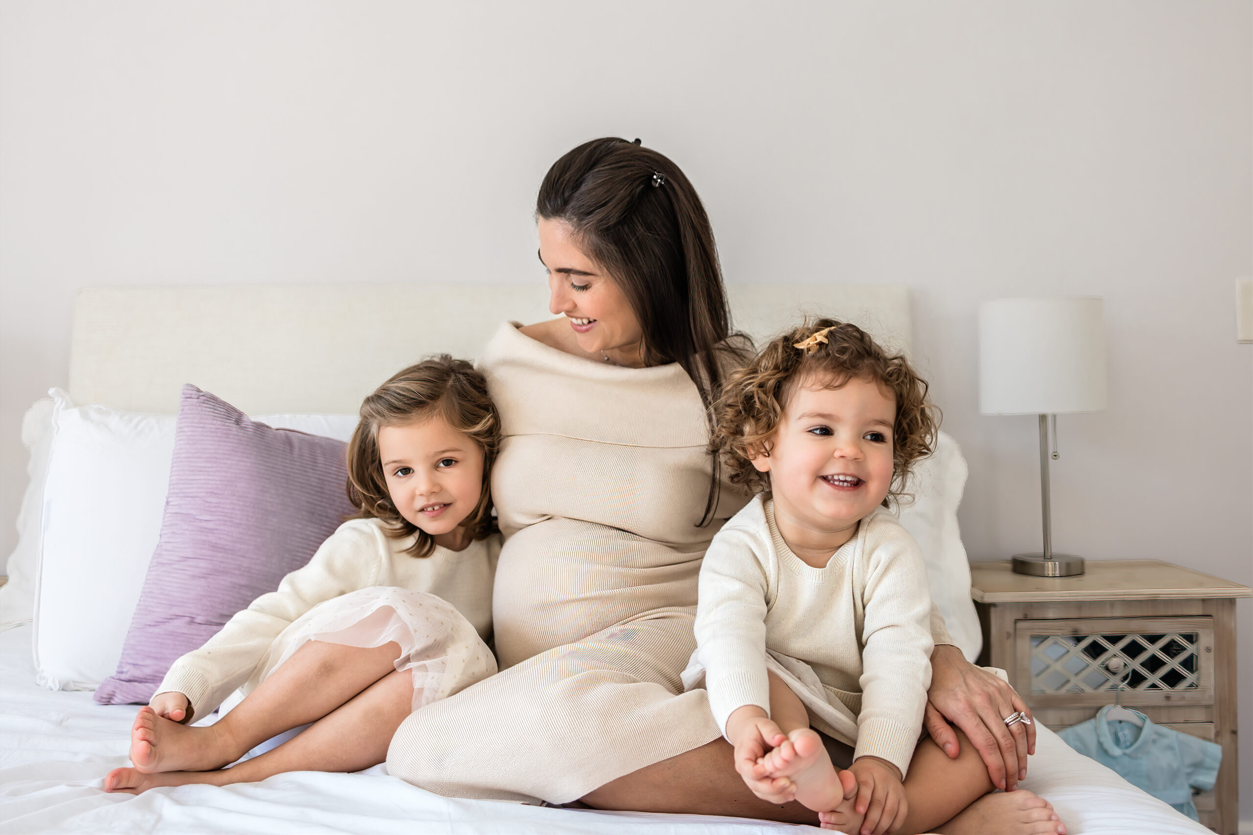 Pregnant woman cuddling two little girls on a bed during a relaxed in-home maternity photo shoot in Scotch Plains NJ