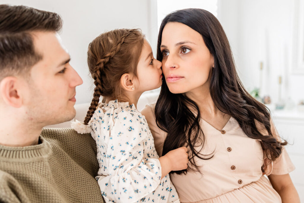 toddler kissing mom on cheek while sitting on bed