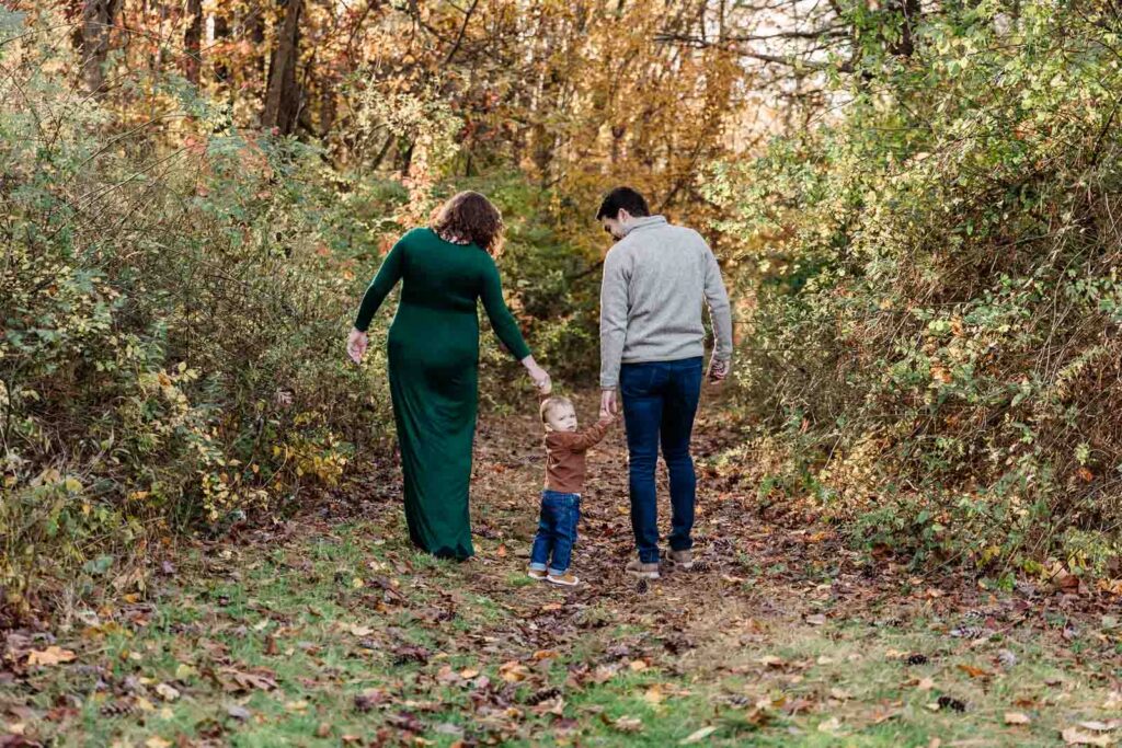 Toddler boy exploring leaves with mom and dad in the woods